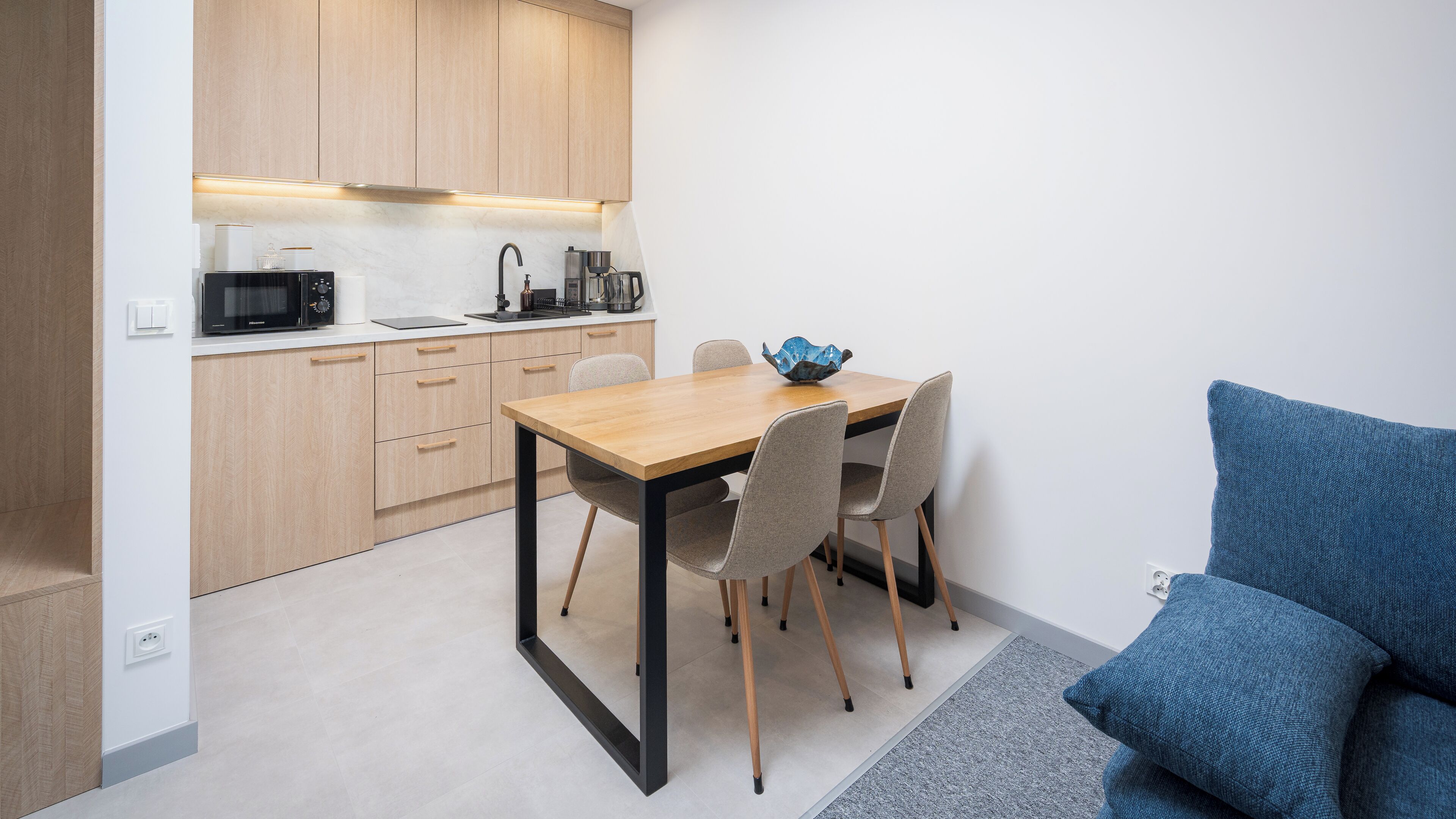 Een compacte keuken met moderne apparaten, een eettafel met stoelen en een blauw kussen.