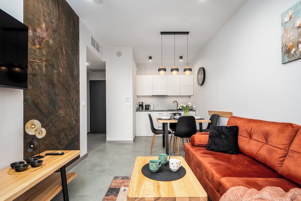 Een moderne woonkamer met een houten salontafel, een rode bank en een keuken op de achtergrond.