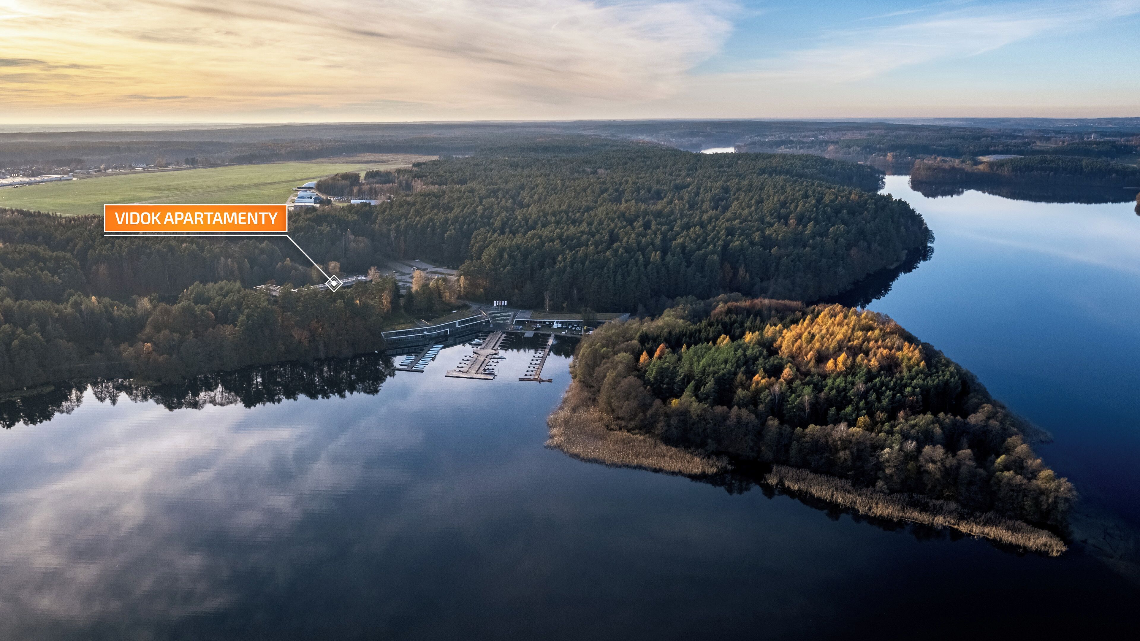 Vue aérienne des appartements Vidok, avec un port de plaisance et le paysage boisé environnant.