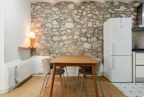 A small kitchen with a stone wall, a white refrigerator, and a wooden table with chairs. - Temporarily out of Booking (Barcelona)
