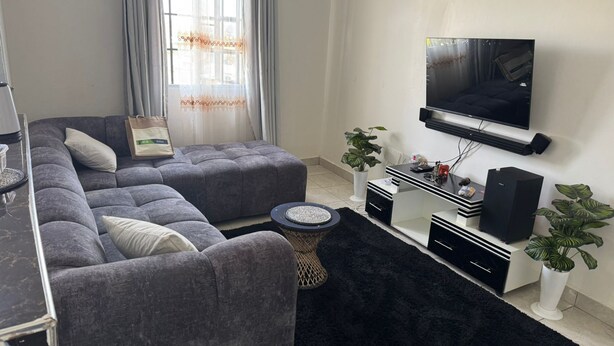 Una sala de estar moderna con un sofá modular, un televisor de pantalla plana en la pared, una mesa de centro y un tapete negro.