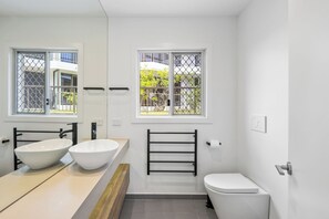 A modern bathroom with two large white sinks, a black towel rack, a toilet, and windows with metal grilles. - Thirty-Nine Albatross (Apartment 3) (Mermaid Beach)