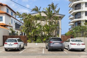 A parking lot with three cars, a building with balconies, and palm trees. - Thirty-Nine Albatross (Apartment 3) (Mermaid Beach)