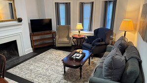Un salon avec une cheminée, un téléviseur, deux fauteuils, un canapé et une table basse.