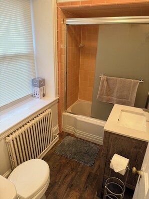 Un baño con inodoro, bañera, ducha, lavamanos y ventana con persianas.