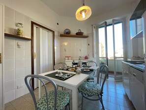 A modern kitchen with white tiles, a dining table with chairs, a hanging light fixture, and a view of the outside through a large window. - Casa Mariò: Cozy apartment on the outskirts of Siena with elevator and AC (Siena)