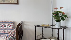 Canto de um quarto com uma cama de madeira, uma mesinha com uma planta e um livro aberto.