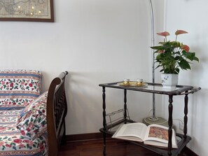 A corner of a room with a wooden bed, a small table with a plant, and an open book. - Casa Mariò: Cozy apartment on the outskirts of Siena with elevator and AC (Siena)