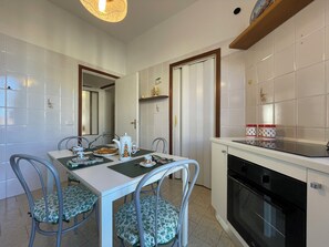 A dining area with a white table, two chairs with green floral upholstery, a white kettle, and a small statue on the wall. - Casa Mariò: Cozy apartment on the outskirts of Siena with elevator and AC (Siena)