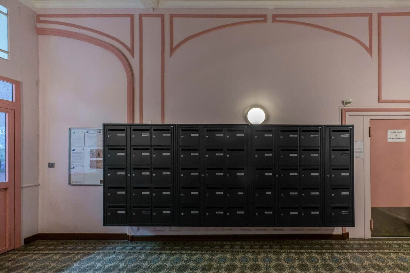 Une pièce dans laquelle se trouve un grand classeur noir, adossé à un mur orné de moulures décoratives roses.
