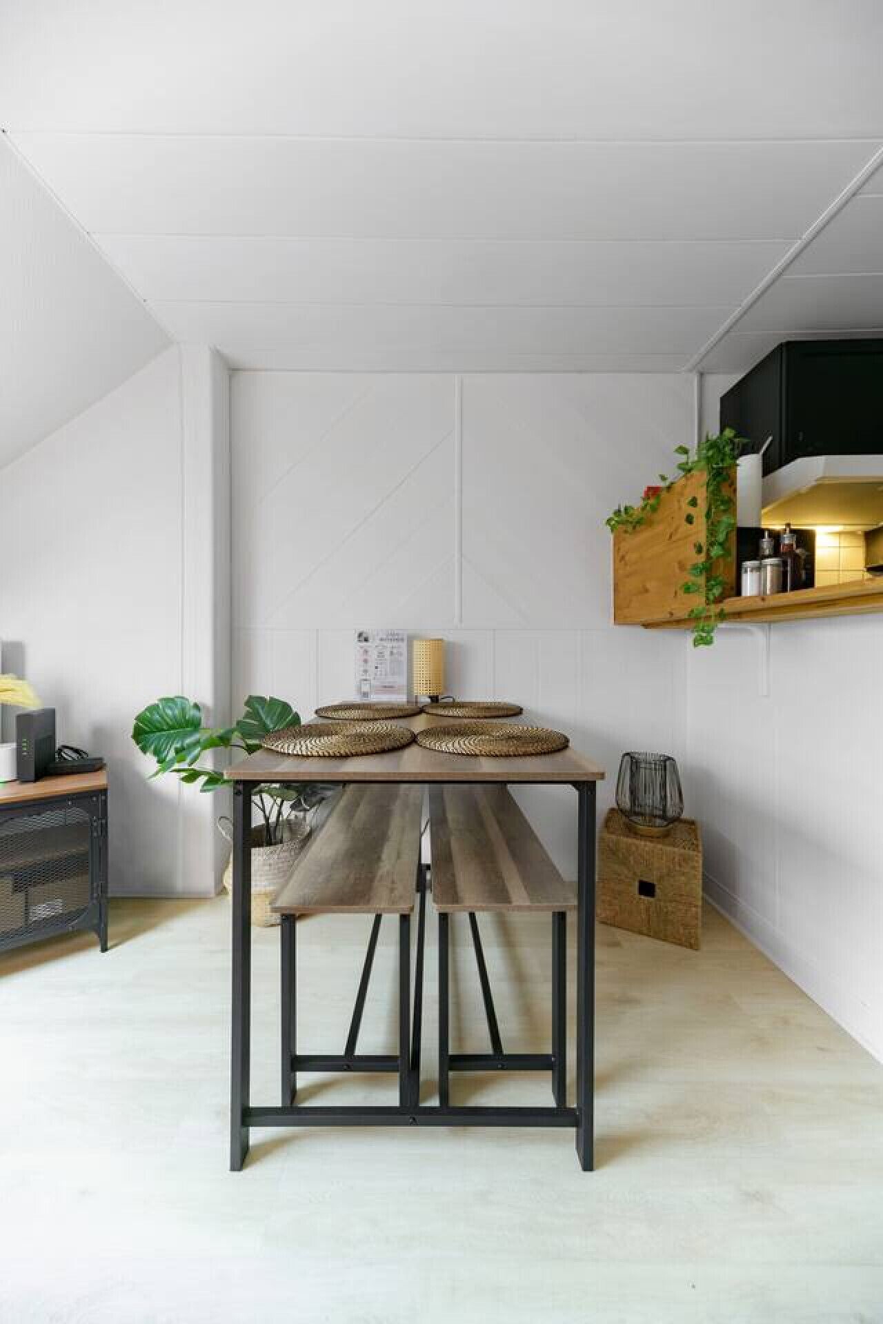 Una cocina compacta con una mesa de madera, una planta colgante y un estante pequeño con utensilios de cocina.