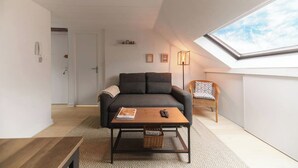 Ein modernes Wohnzimmer mit einem dunkelgrauen Sofa, einem Holztisch und einem Korbstuhl.