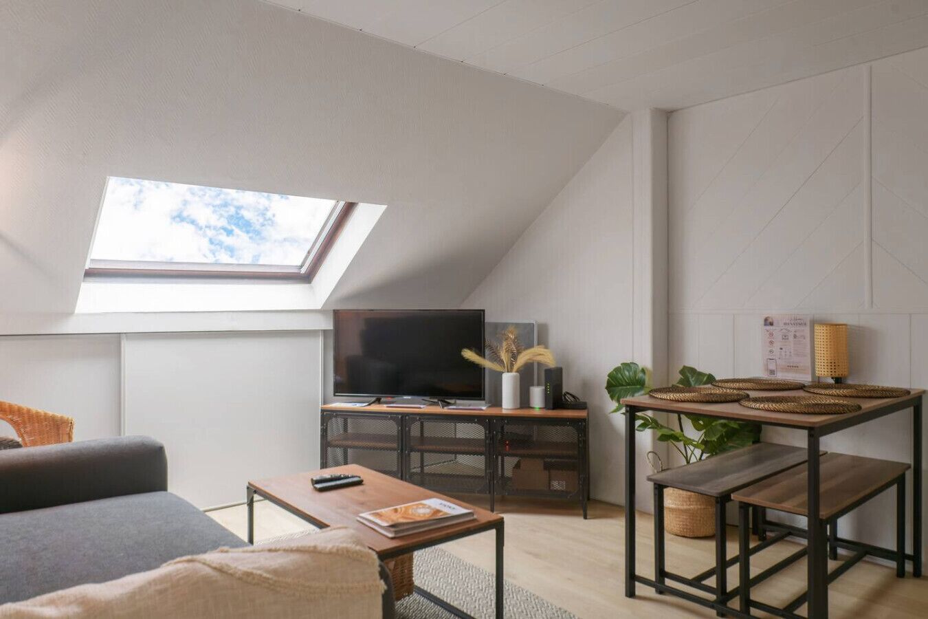 Un dormitorio tipo loft moderno con tragaluces, televisor, escritorio y una zona de estar cómoda.