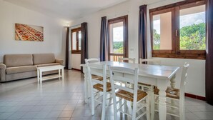 Ein Essbereich mit weißem Tisch und Stühlen, einem beigen Sofa und Blick auf Grün hinter großen Fenstern.