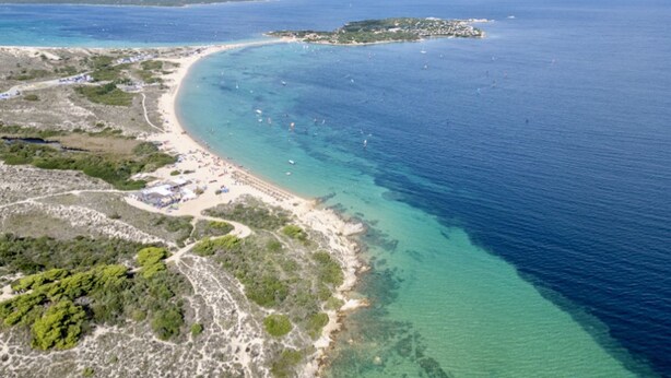 Eine Luftaufnahme einer Küstenregion mit Strand, klarem Wasser und einer kleinen Insel in der Ferne.