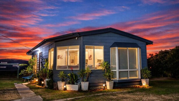 Una casa moderna con ventanas amplias, un porche cubierto y plantas en macetas.