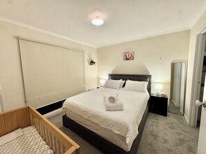 Ein ordentlich eingerichtetes Schlafzimmer mit einem großen Bett, Nachttischen, einem Holckrippenbett und einer Deckenleuchte.