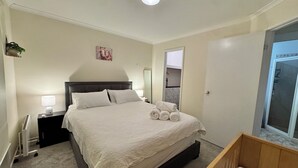 Un dormitorio con cama, mesitas de noche, radiador, espejo, ventana y puerta.