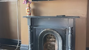 A fireplace with a TV mounted above it, a vase with flowers on the mantel, and a wooden floor. - GREAT VALUE COMFORT WITH THE PERFECT LOCATION! (Redfern)
