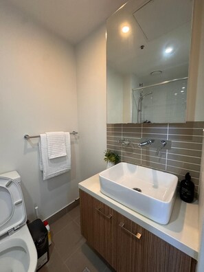 A modern bathroom with a white sink, wooden cabinet, and a large mirror above the sink. - Sweet Home-Style Comfort 2B2B Apartment in Central (Melbourne)