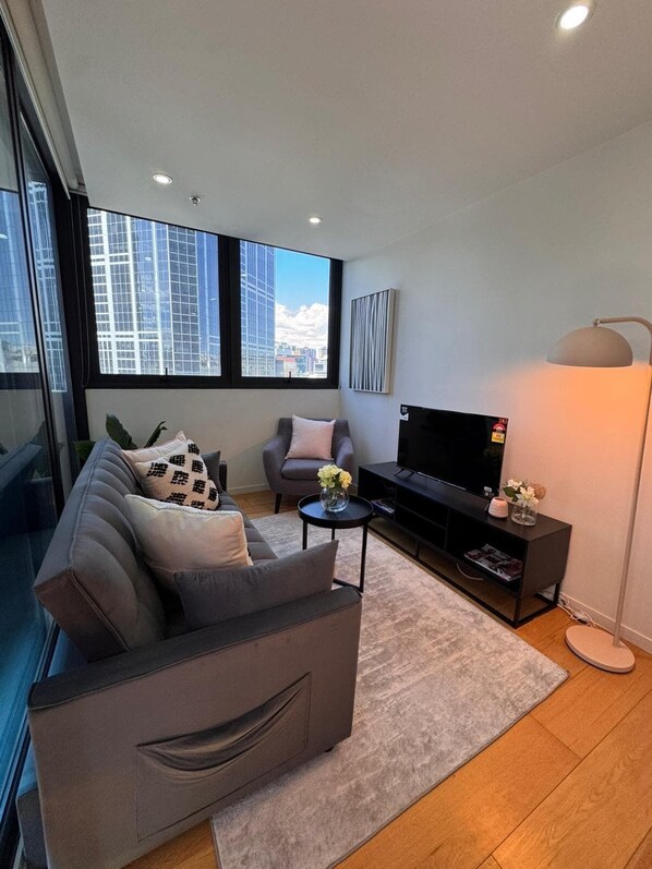 A modern living room with a sofa, armchair, and TV, large windows with a city view, and a floor lamp. - Sweet Home-Style Comfort 2B2B Apartment in Central (Melbourne)