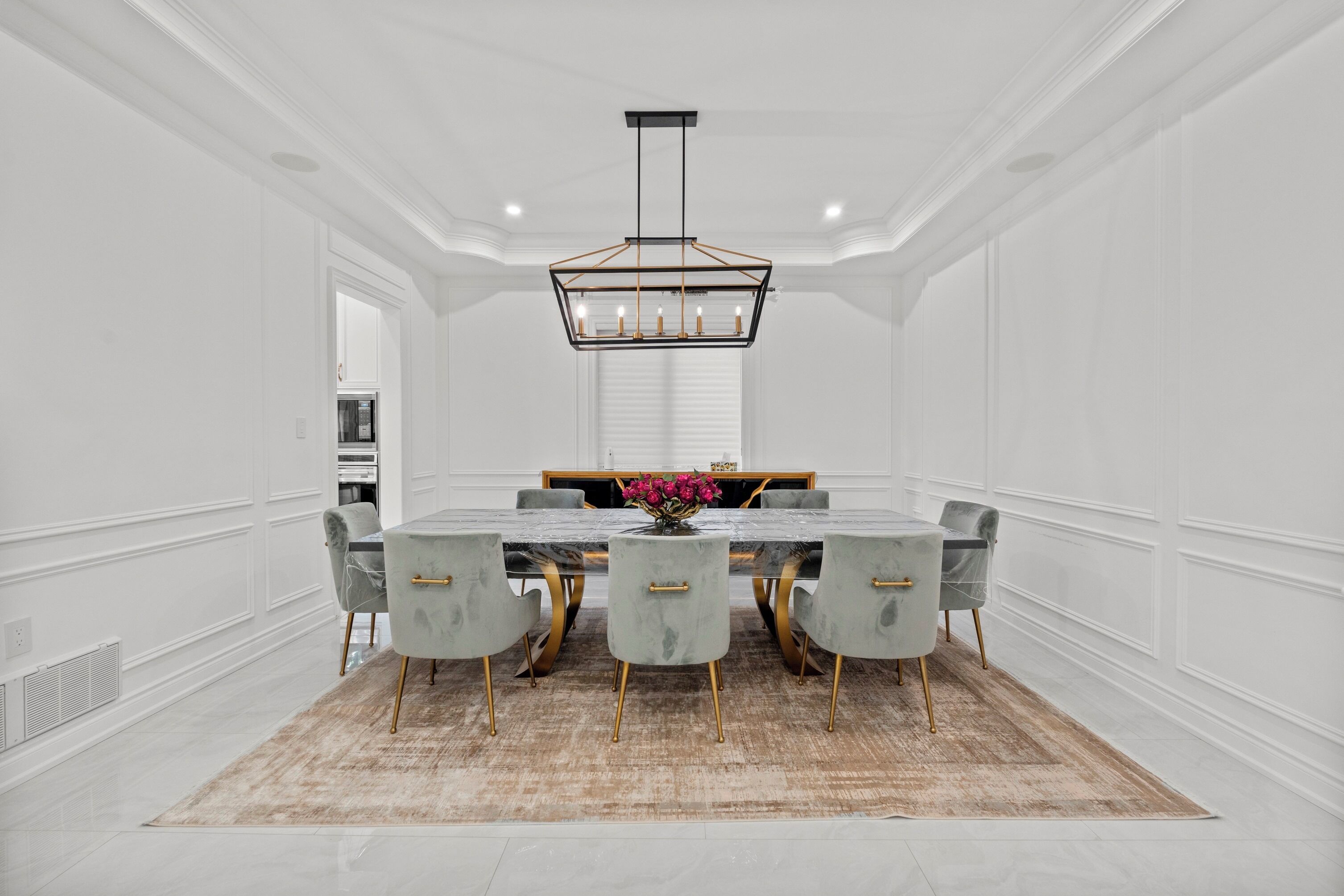 A dining room with a marble table, grey upholstered chairs, and a chandelier.