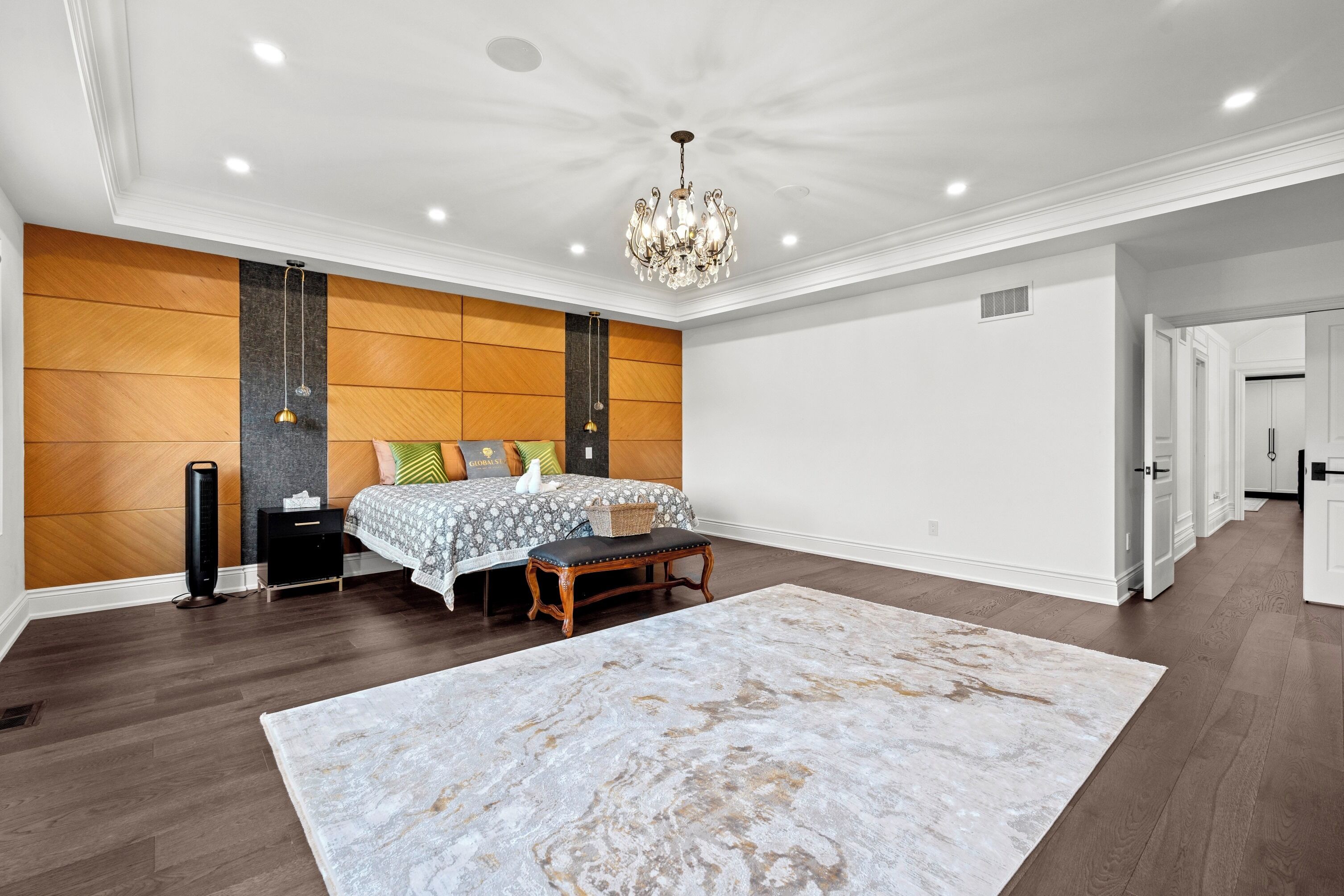 A spacious bedroom with a large bed, a chandelier, and a wooden accent wall.