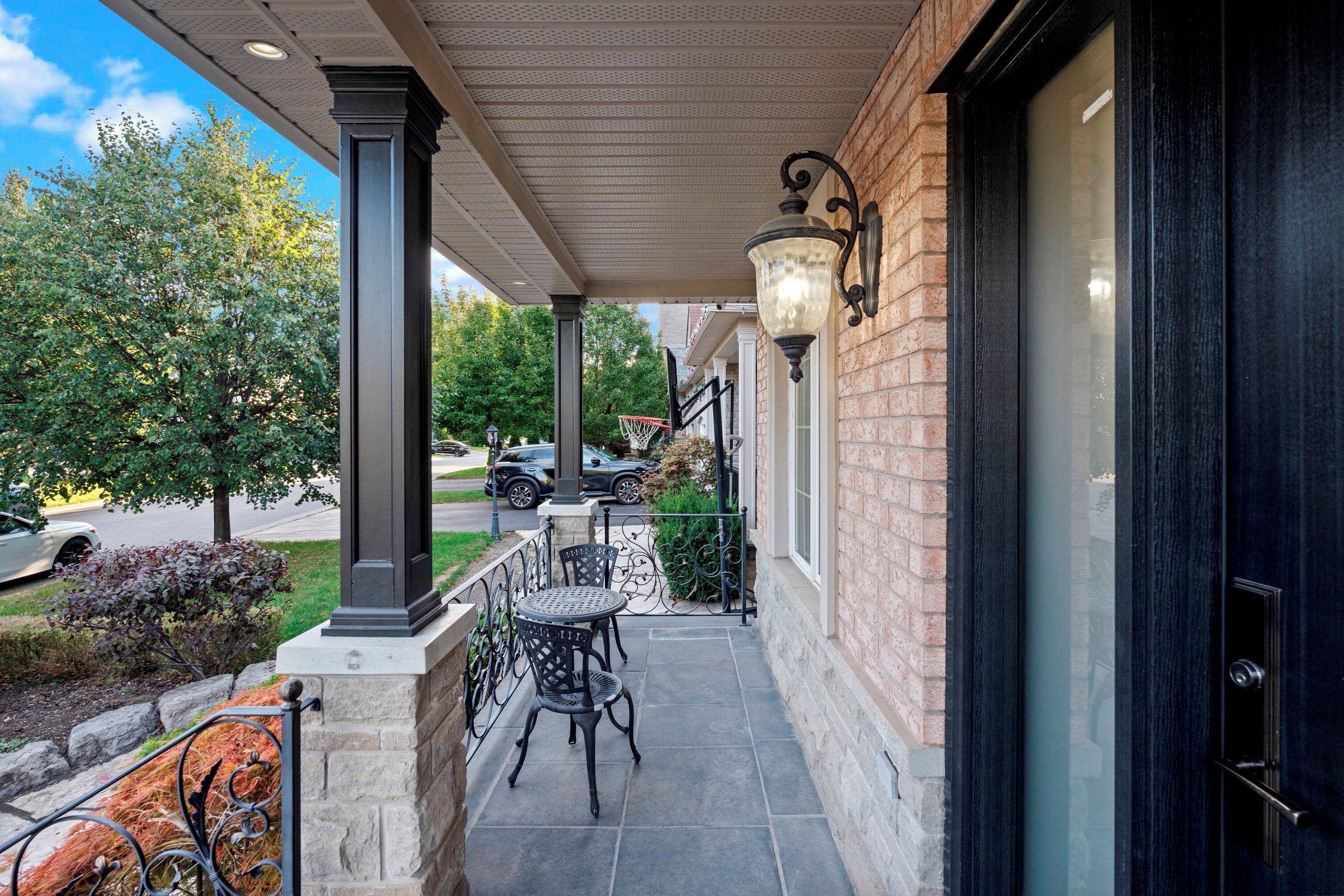 A covered outdoor area with a brick wall, a black door, and a small patio with two metal chairs and a table.