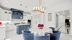 Une cuisine moderne avec des meubles blancs, un mur d’accent bleu et une table à manger ronde entourée de chaises bleues.