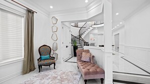 Un vaste espace de vie agrémenté d’un canapé moelleux, d’un fauteuil à motifs et d’un tapis duveteux. Un escalier avec une rampe noire mène à l’étage supérieur.