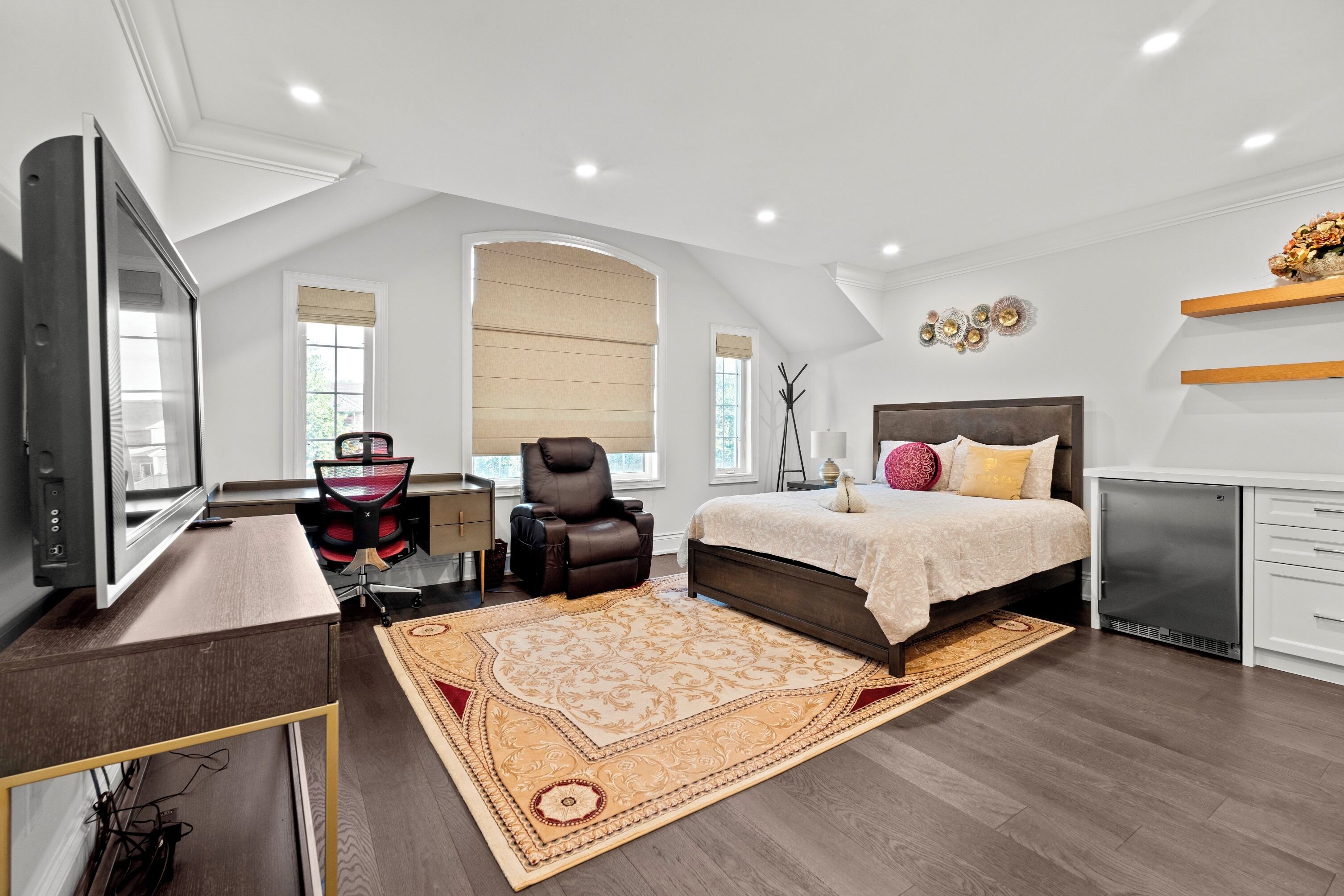 A modern bedroom with a large bed, a desk, and a TV.