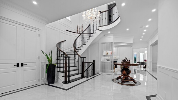 Un hall d’entrée spacieux, agrémenté d’un magnifique escalier, d’un lustre et d’un plancher poli.