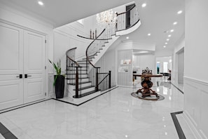 Un hall d’entrée spacieux, agrémenté d’un magnifique escalier, d’un lustre et d’un plancher poli.