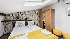 A bedroom with a skylight, a large bookshelf, a bed with yellow bedding, and a wooden wardrobe. - Apartamenty Sun & Snow Sunshine Loft (Kraków)