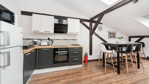 A modern kitchen with a wooden ceiling, white cabinets, and a dining area with black chairs. - Apartamenty Sun & Snow Sunshine Loft (Kraków)