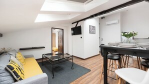 A modern living room with a glass dining table, a sofa with yellow cushions, and a view of the kitchen through an open door. - Apartamenty Sun & Snow Sunshine Loft (Kraków)
