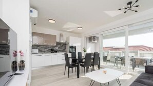 Une cuisine moderne avec des meubles blancs, un coin repas avec une table blanche et des chaises noires, et un balcon avec un espace salon extérieur.