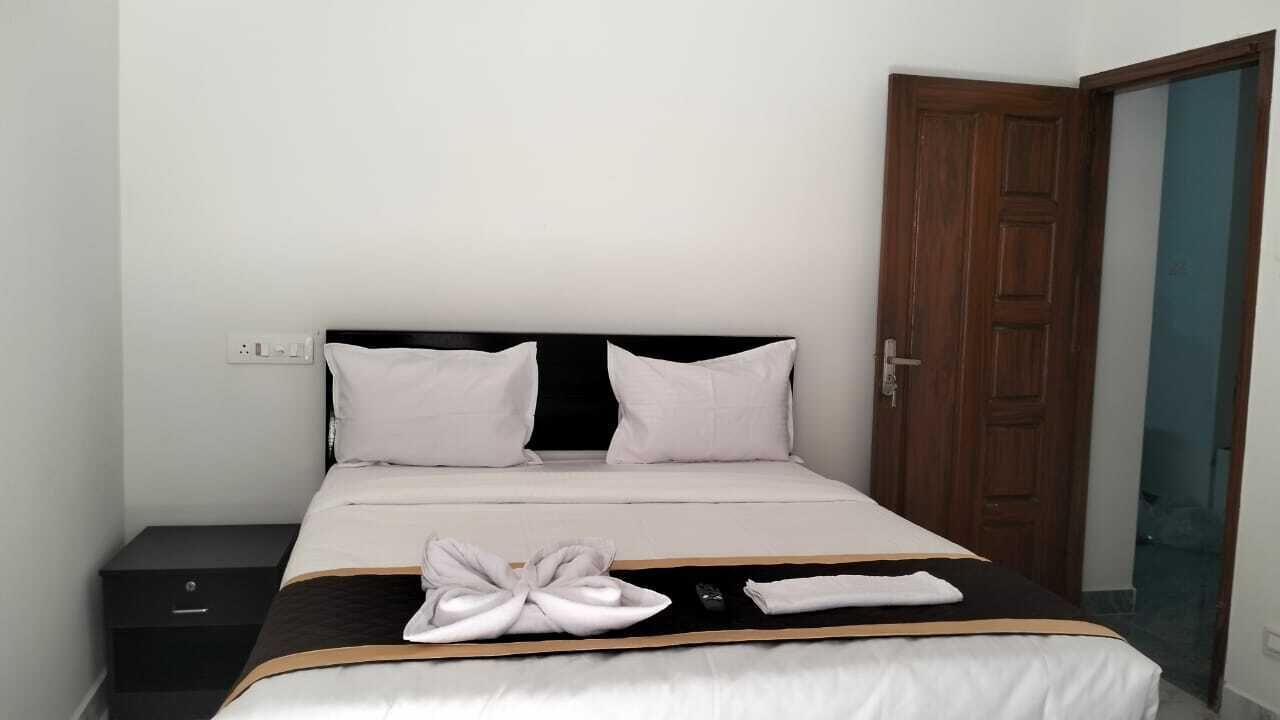 A neatly made bed with white linens and a black headboard, a wooden door, and a small bedside table with a black drawer.