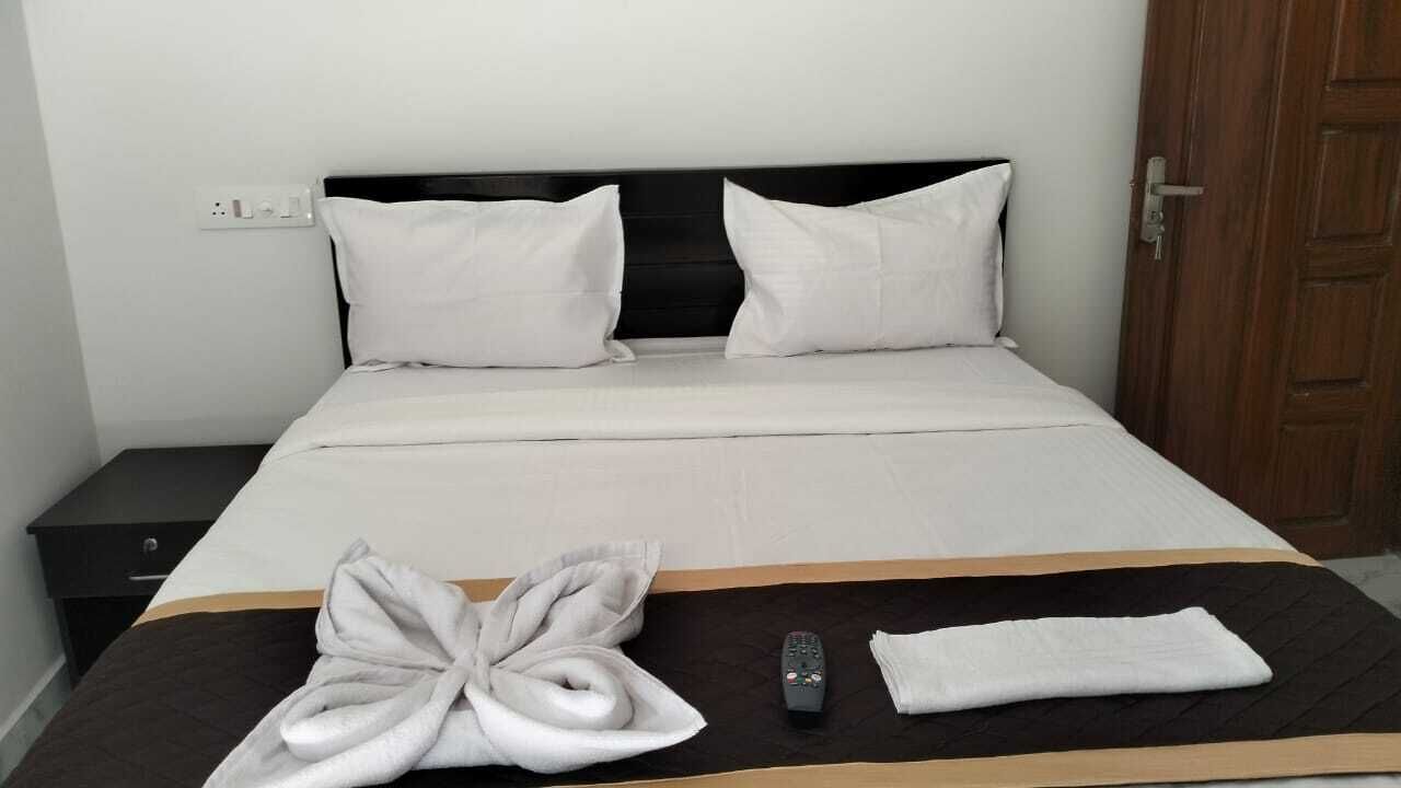 A neatly made bed with white linens, a remote control, and a folded towel on a dark bedspread.