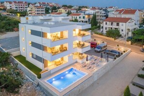 Um edifício moderno com vários andares, piscina no terraço e área externa para sentar.