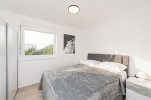 Um quarto com uma cama, mesa de cabeceira, janela e luminária fixada na parede.