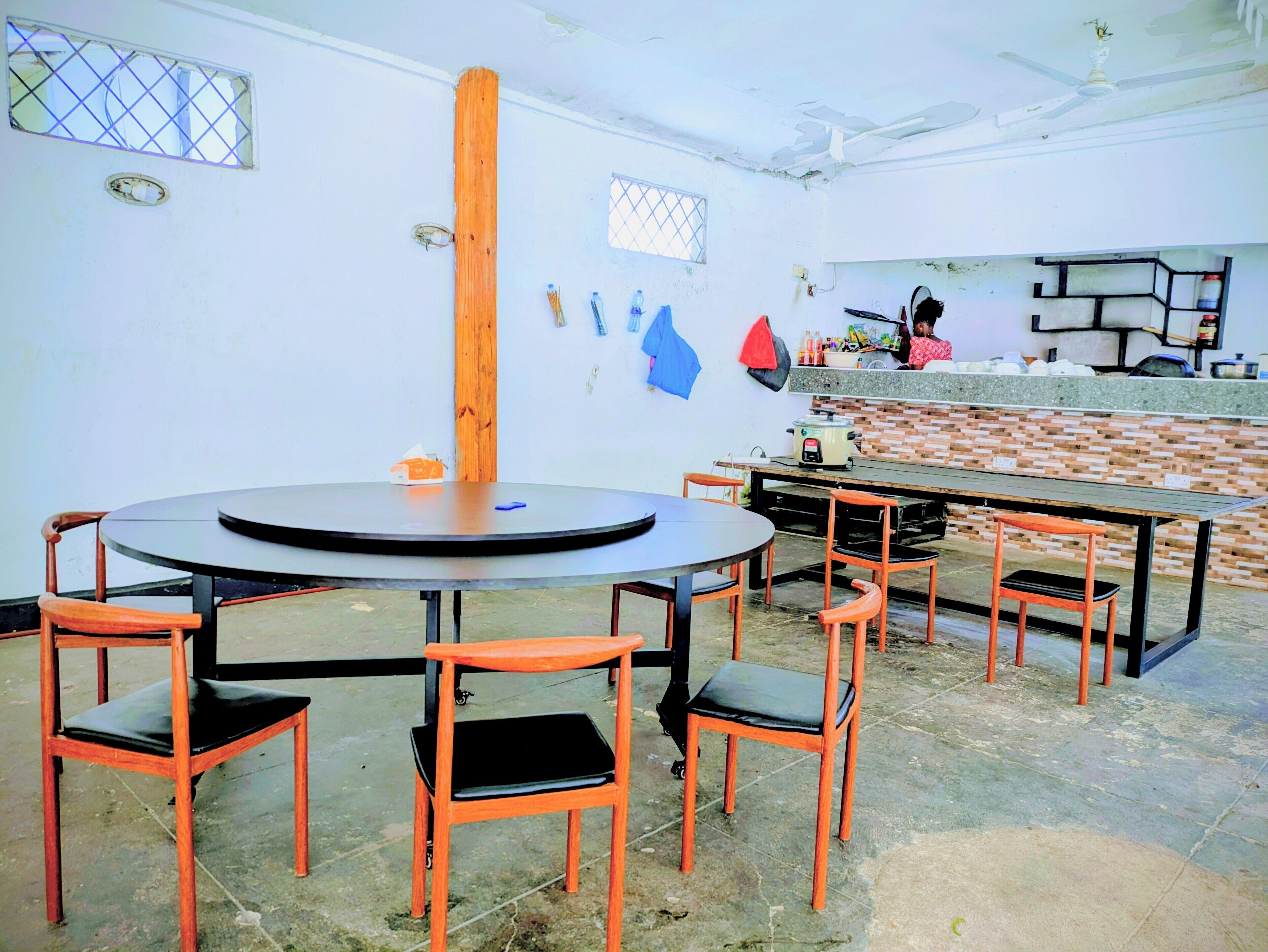 A dining area with a round table and six chairs, a kitchen counter, and a person in the background.