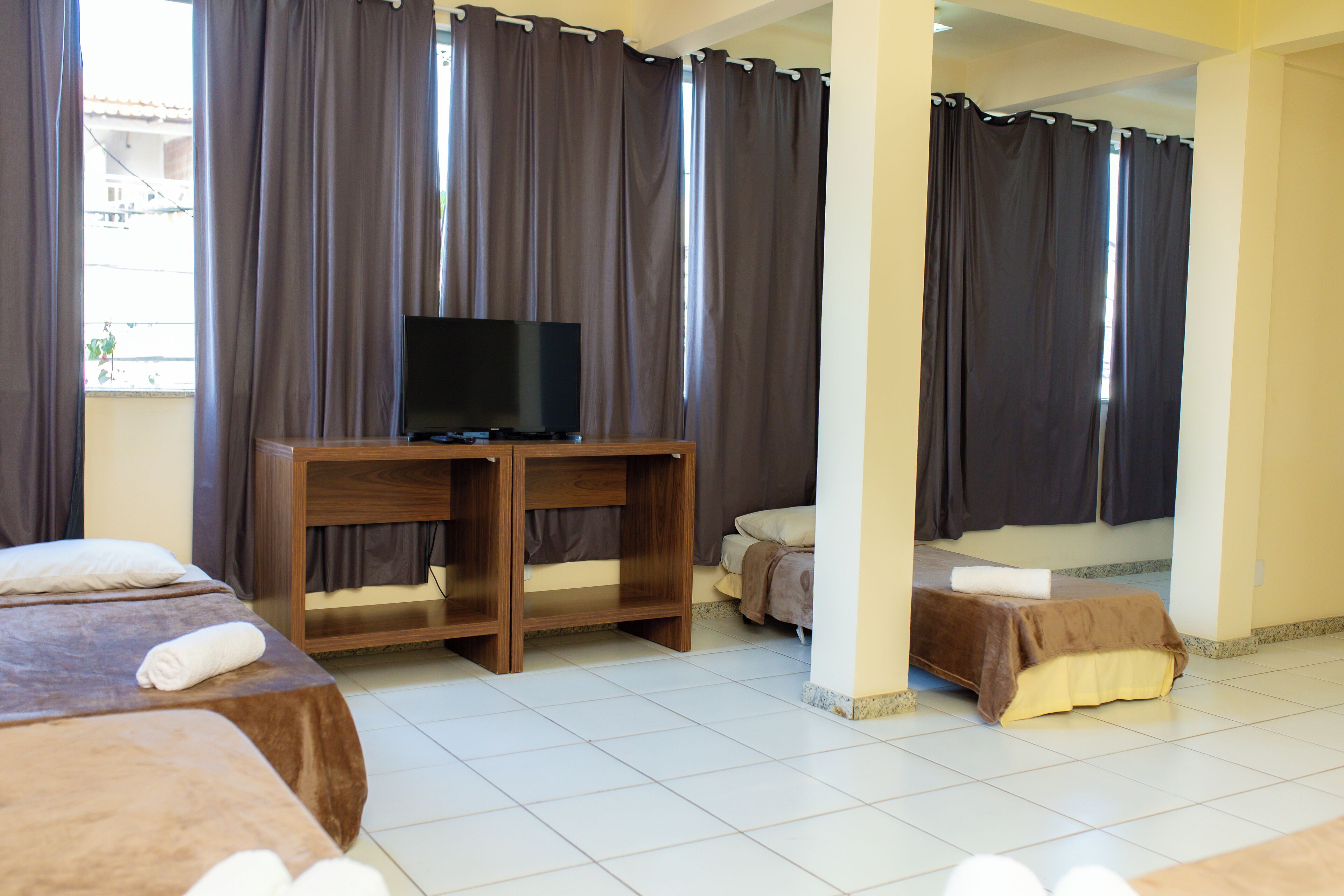 A hotel room with a bed, a TV on a wooden stand, and a window with curtains.