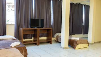 A hotel room with a bed, a TV on a wooden stand, and a window with curtains.