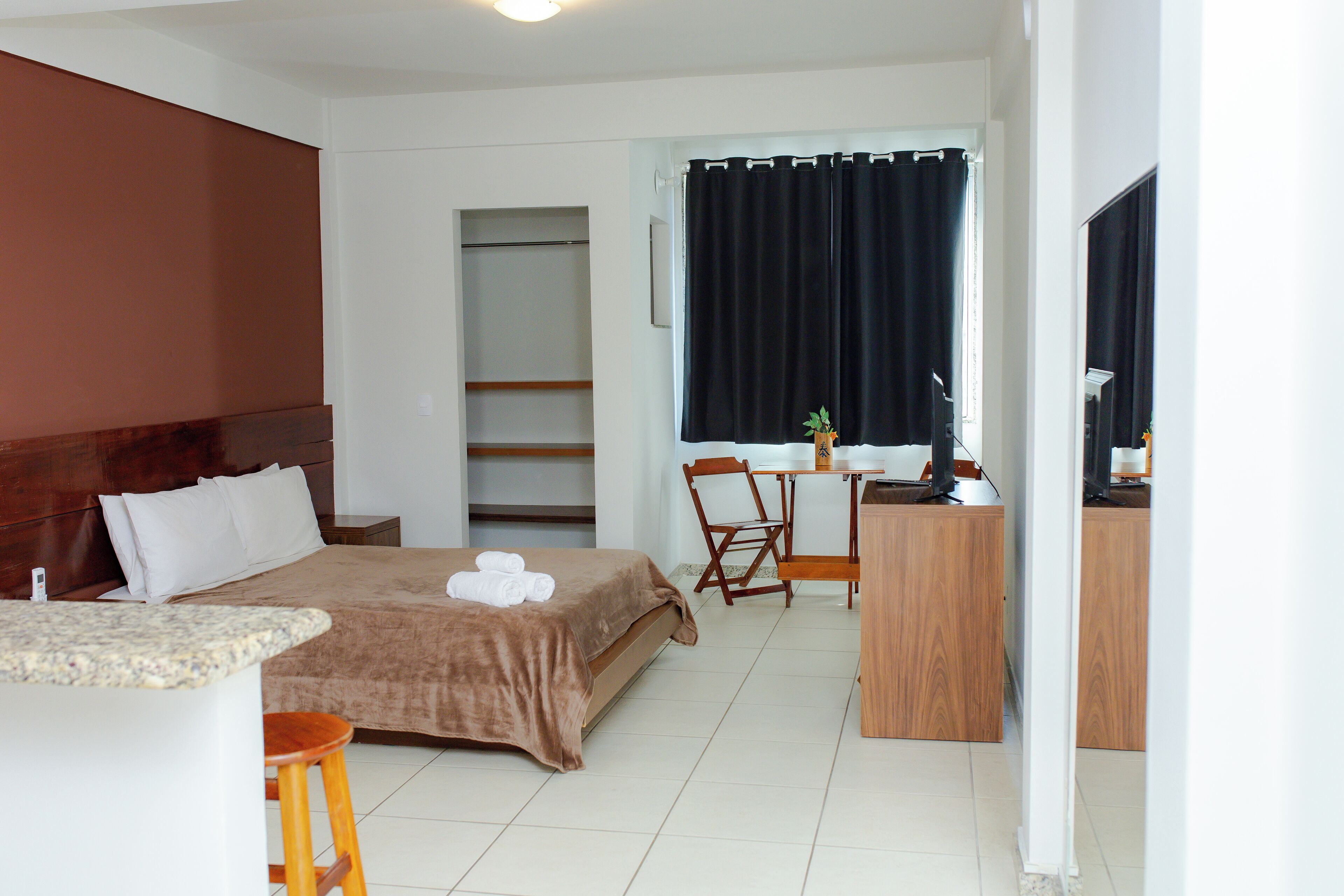 Una habitación de hotel con cama, escritorio, silla, mesita y ventana con cortinas.