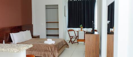 A hotel room with a bed, a desk, a chair, a small table, and a window with curtains.