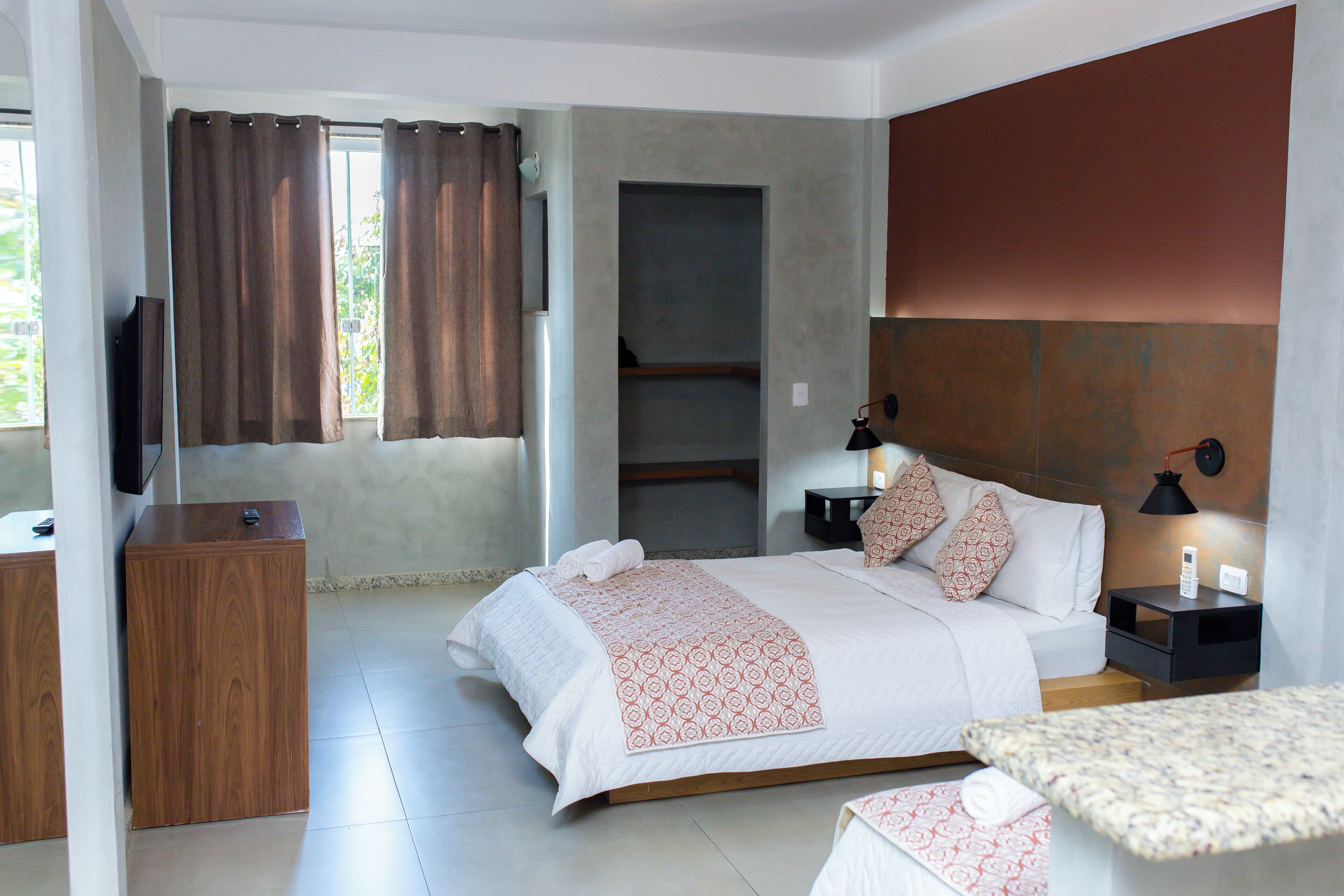 A modern hotel room with a bed, bedside tables, a TV, and a window with curtains.