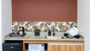 A kitchen with a granite countertop, a coffee maker, a microwave, a sink, and a dish rack. - Pousada Caiçara Flats (Cabo Frio)