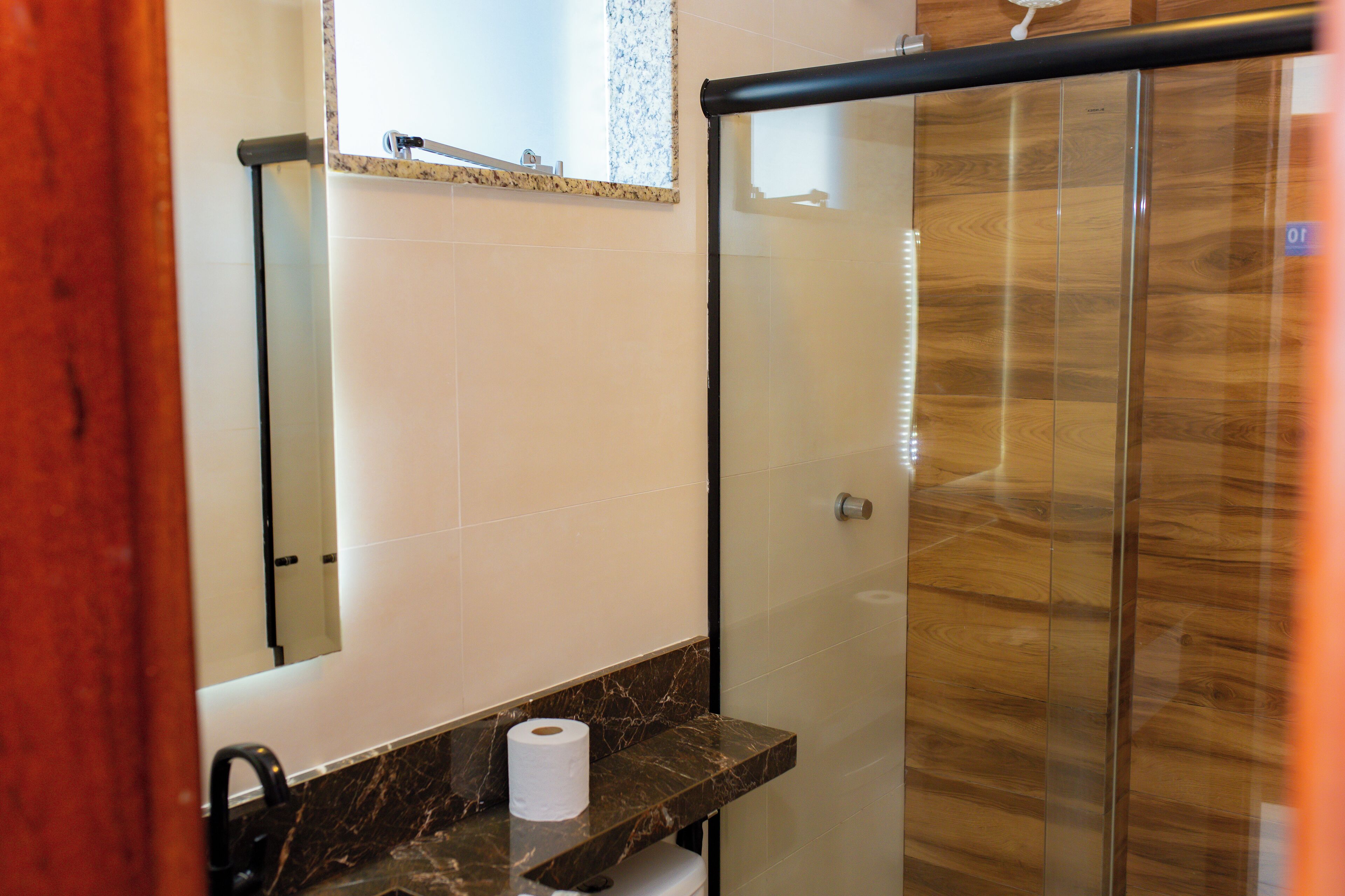 A bathroom with a marble countertop, a toilet paper roll, and a glass shower enclosure.