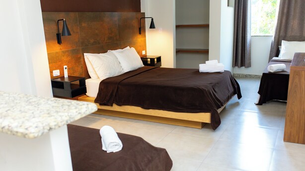 A modern hotel room with a large bed, bedside tables, a wooden headboard, and a small desk area. - Pousada Caiçara Flats (Cabo Frio)